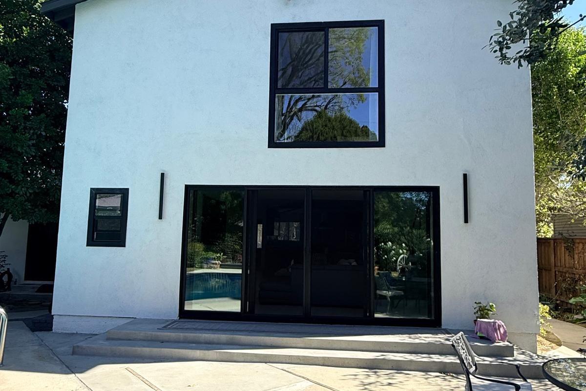 Two storey white house with black framed glass and the pool alongside